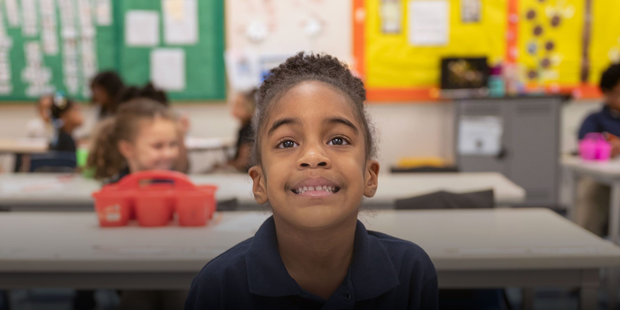 Smiling elementary student sitting at a desk in a classroom.